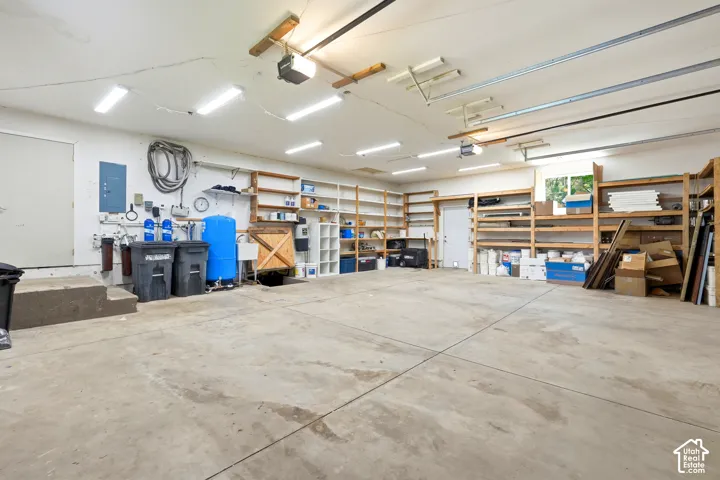 Spacious garage featuring a concrete floor, abundant overhead fluorescent lighting, and extensive built-in shelving for organization