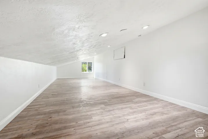 Expansive loft space featuring wood-finish flooring, recessed lighting, and a window providing natural light