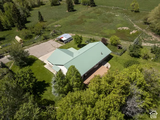 Expansive property featuring a residence with a green metal roof, a substantial paved driveway, and a large wood-finish deck