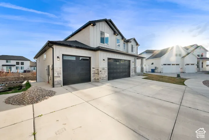 View of side of property featuring driveway, board and batten siding, an attached garage, and stone siding