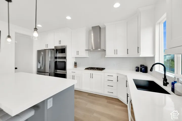 Kitchen with light wood-type flooring, stainless steel appliances, hanging light fixtures, decorative backsplash, and light stone countertops