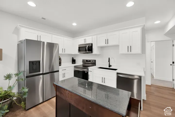 Dual tone kitchen with stainless steel appliances, dark stone counters, light wood finished floors, a kitchen island, and recessed lighting