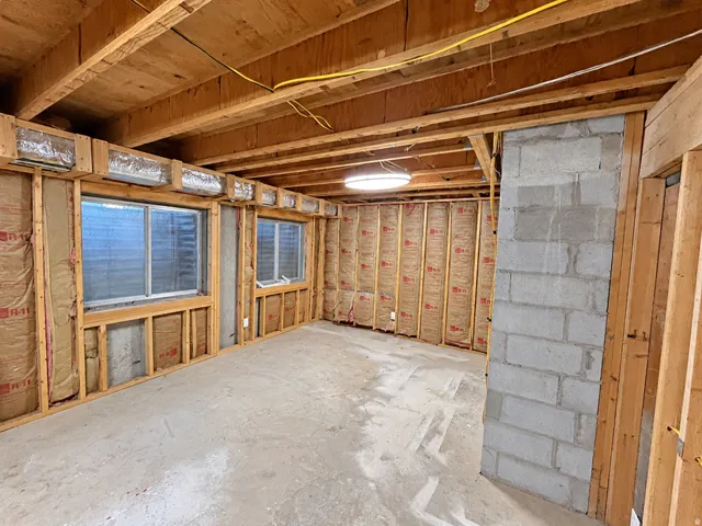 Unfinished basement featuring exposed wood joists, concrete block wall, and two sliding windows
