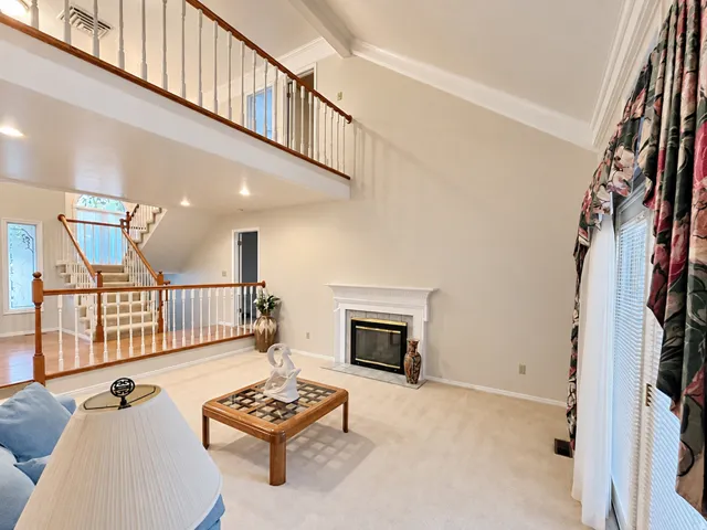 Vaulted ceilings with crown molding, a gas fireplace with a classic mantel, and a two-story open-concept design featuring a staircase with wood-finish railing