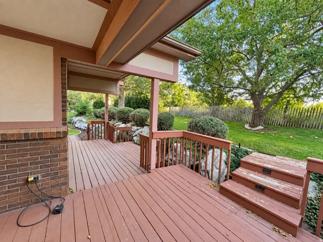 Expansive multi-level wood deck, partially covered, offering direct access to the landscaped yard with mature trees and a wood fence