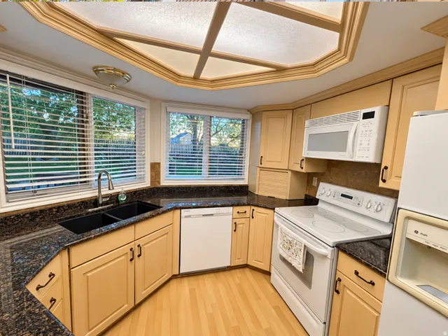 Kitchen with wood-finish flooring, custom cabinetry, dark speckled countertops, and a dual basin sink with a gooseneck faucet