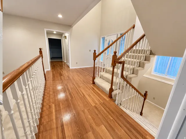 Hardwood flooring, carpeted staircase with white balusters, wooden handrails, recessed lighting, and a white paneled door