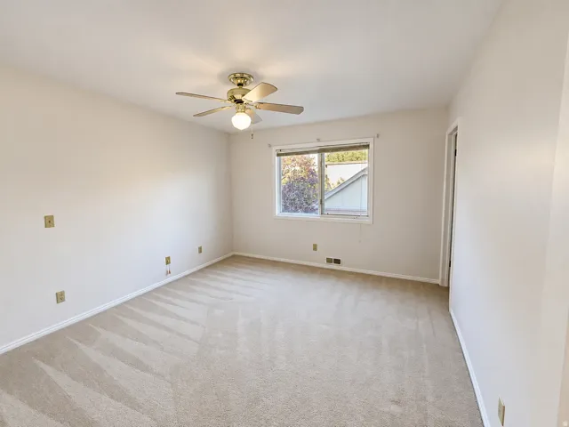 Neutral-toned carpet flooring with a window offering natural light, and a ceiling fan with integrated lighting