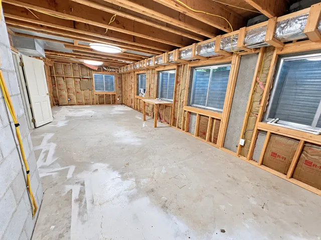 Unfinished interior featuring exposed wood framing, concrete flooring, multiple windows, and two ceiling-mounted light fixtures
