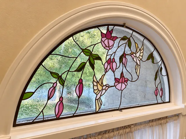 Arched transom window featuring stained glass with hummingbird and floral motifs