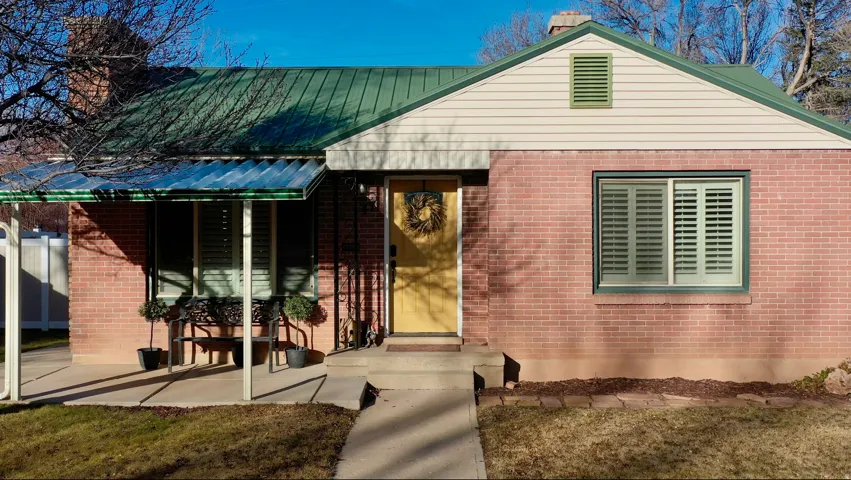 View of front of home with a chimney, brick siding, and a metal roof