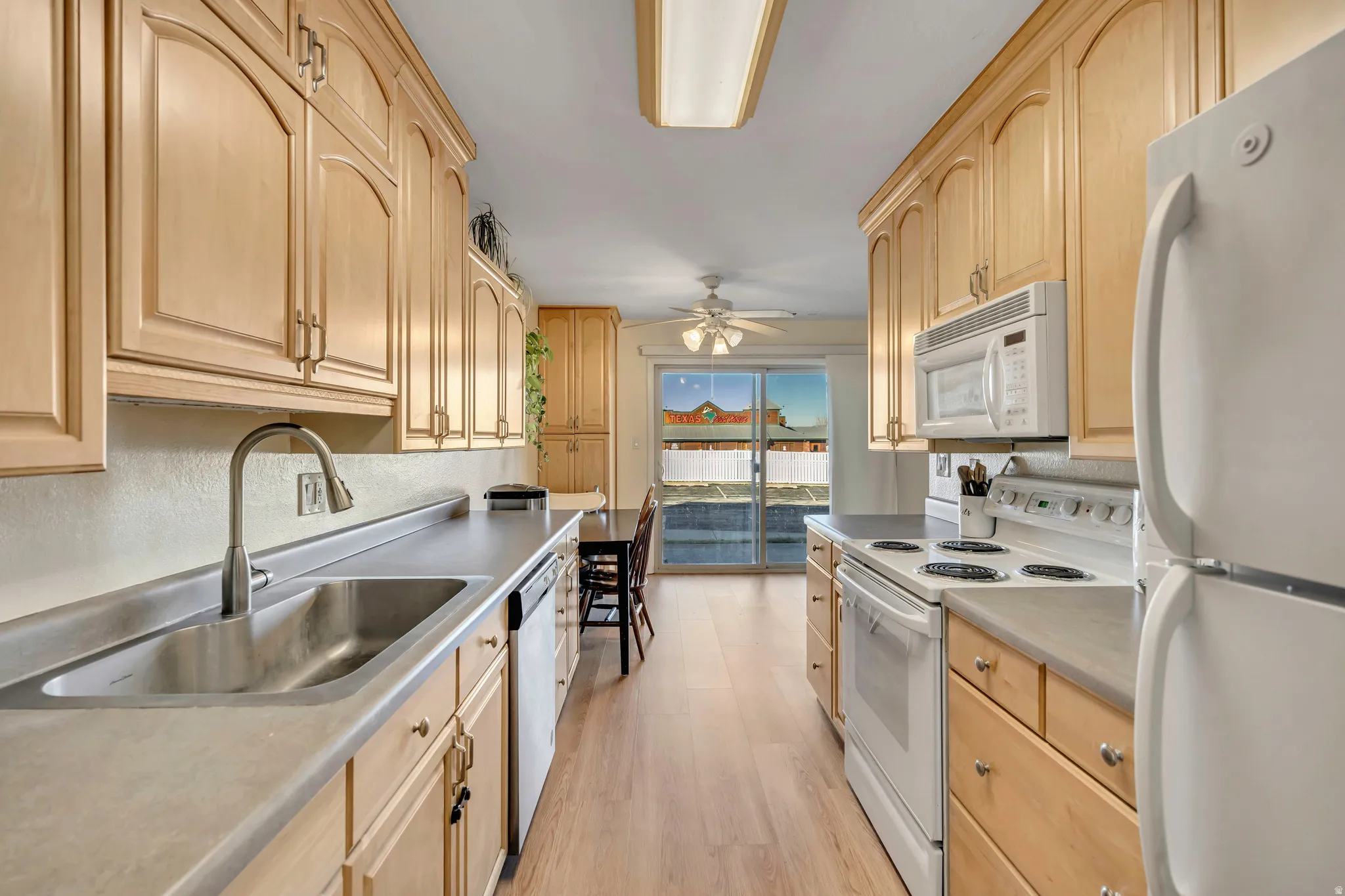 Kitchen with light wood finish cabinets, white appliances, light wood finished floors, and light countertops