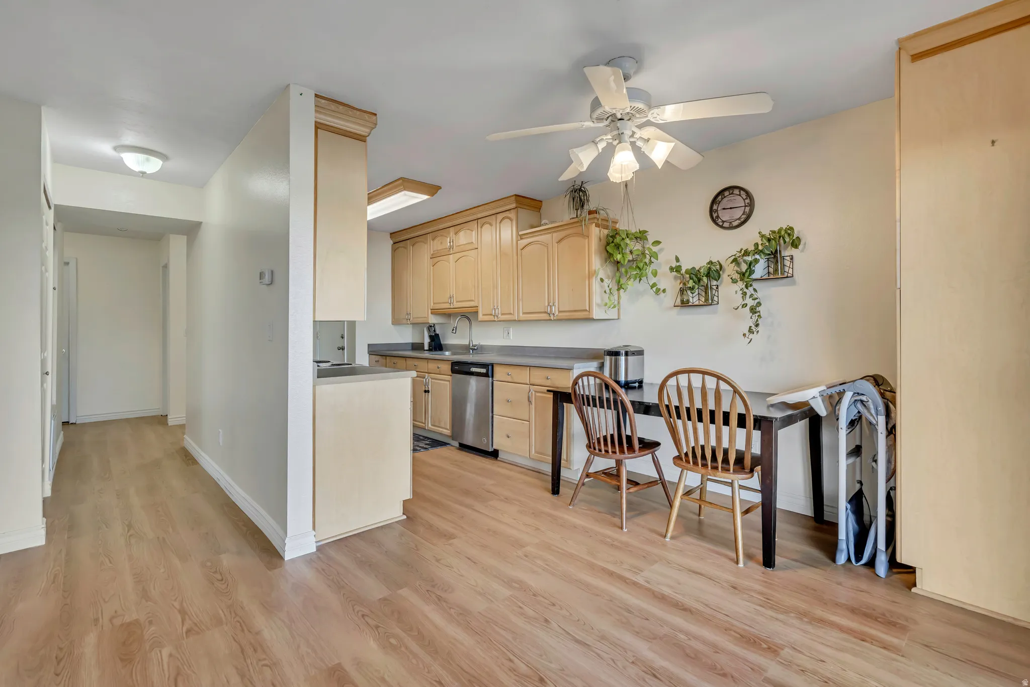 Kitchen featuring light wood finish cabinets, light wood-type flooring, a ceiling fan, dishwasher, and dark countertops