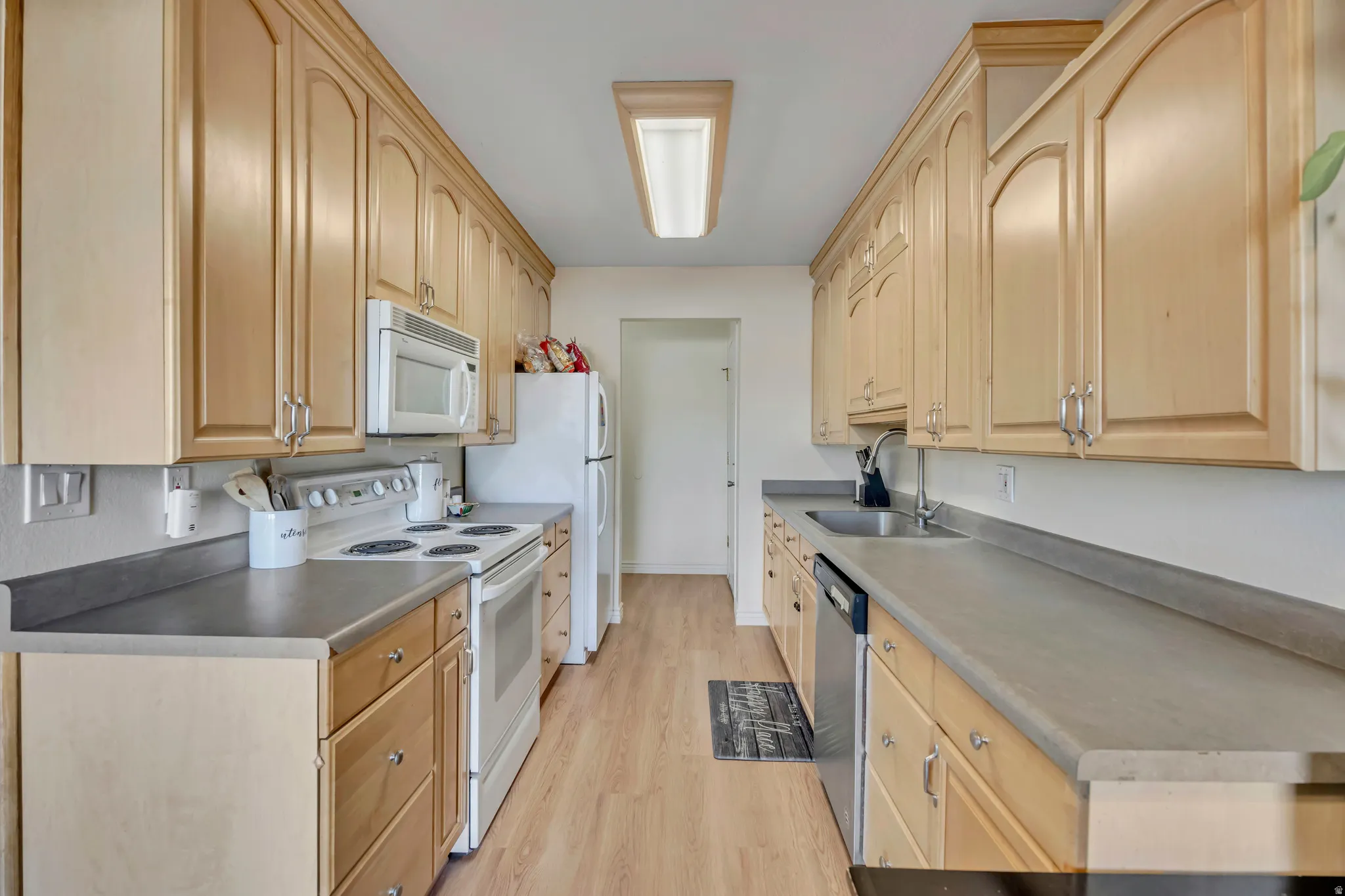 Kitchen featuring white appliances, light wood finish cabinets, and light wood finished floors