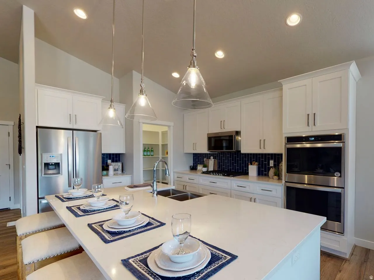 Kitchen with light wood-type flooring, a kitchen bar, stainless steel appliances, white cabinets, and a kitchen island with sink