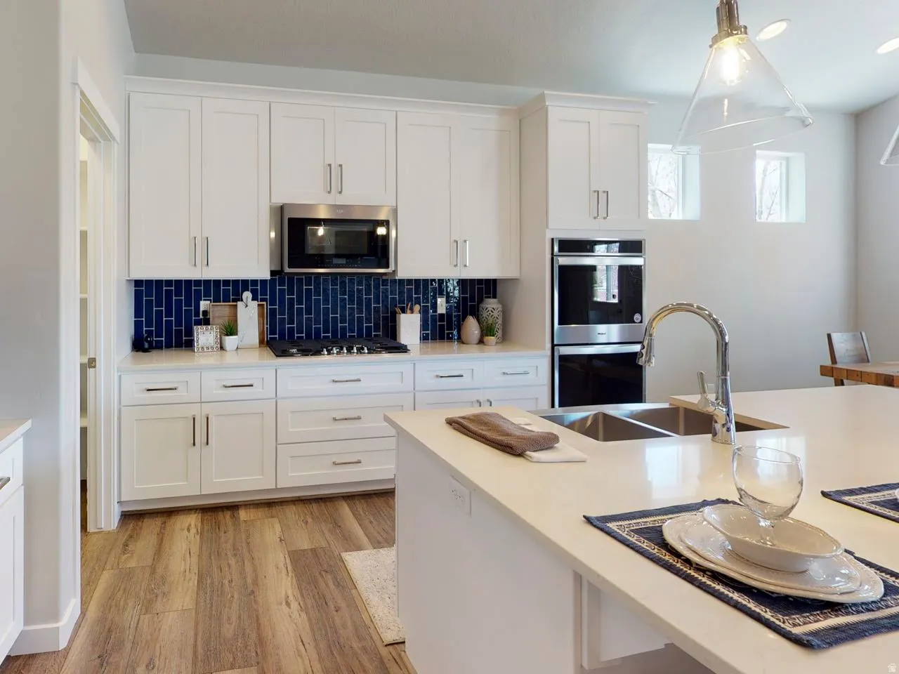 Kitchen with white cabinets, stainless steel appliances, light wood-style floors, hanging light fixtures, and backsplash