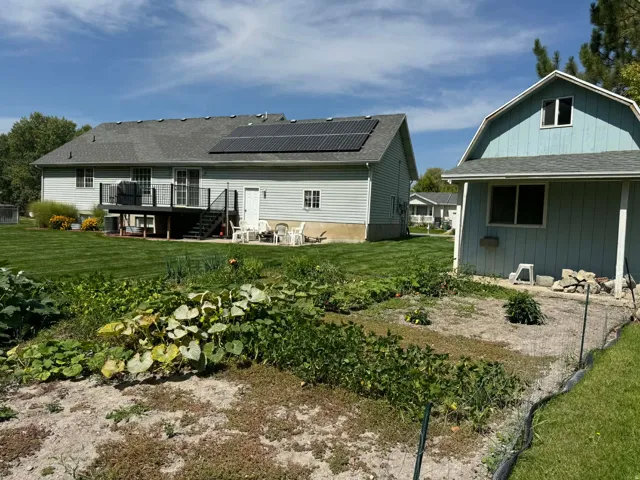 Rear view of house with a shingled roof, solar panels, a yard, a deck, and a gambrel roof