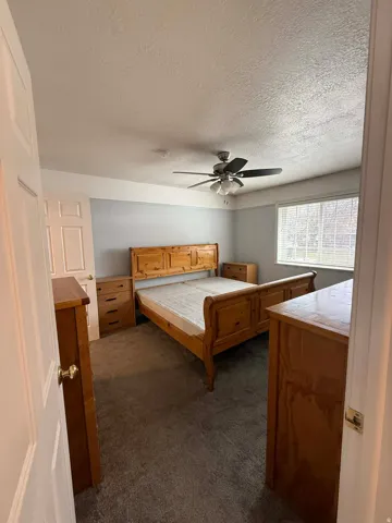 Bedroom with dark carpet, ceiling fan, and a textured ceiling