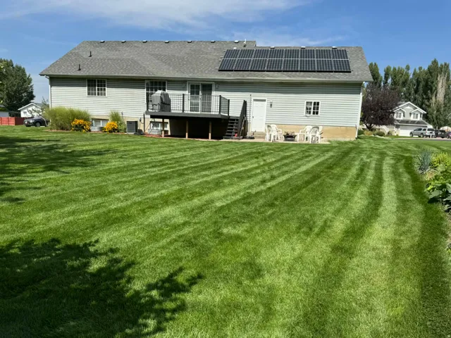 Rear view of property featuring a deck, a lawn, roof mounted solar panels, and a shingled roof