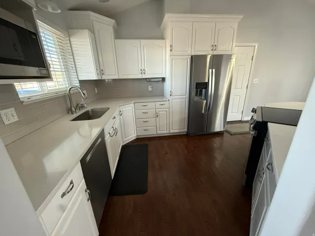 Kitchen with stainless steel appliances, white cabinets, backsplash, and vaulted ceiling
