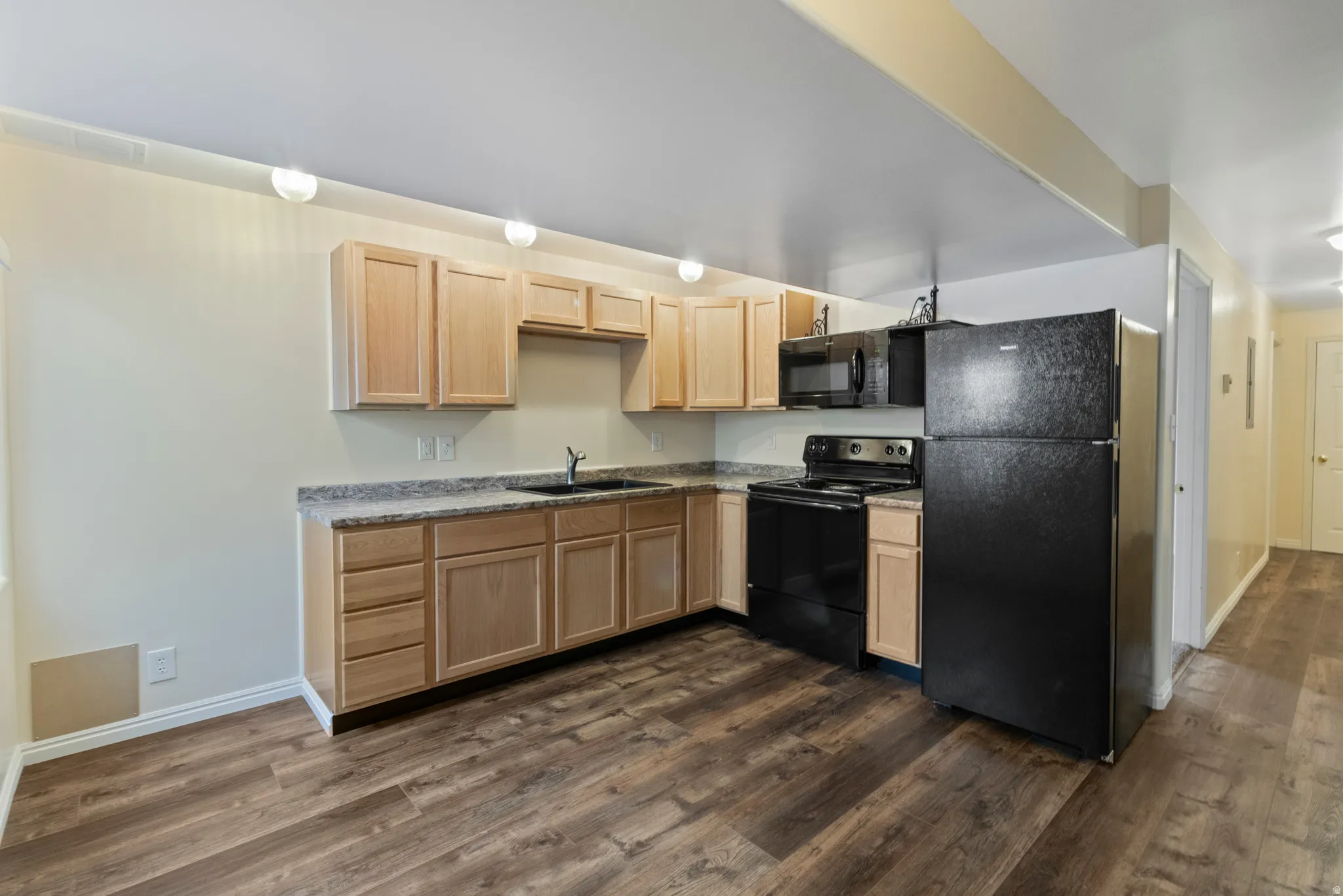 Kitchen featuring light wood finish cabinetry, black appliances, dark wood-style flooring, and light countertops
