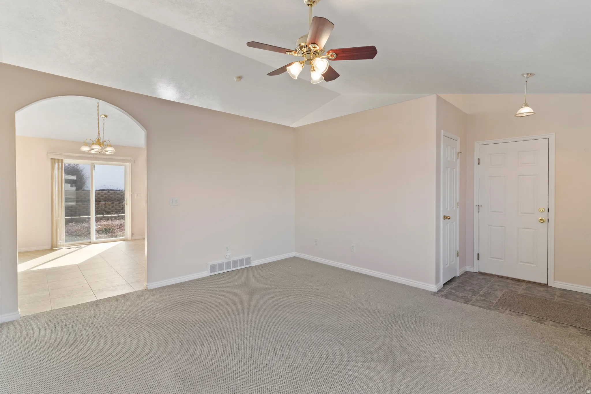 Unfurnished room featuring light colored carpet, arched walkways, a ceiling fan, lofted ceiling, and suspended lighting