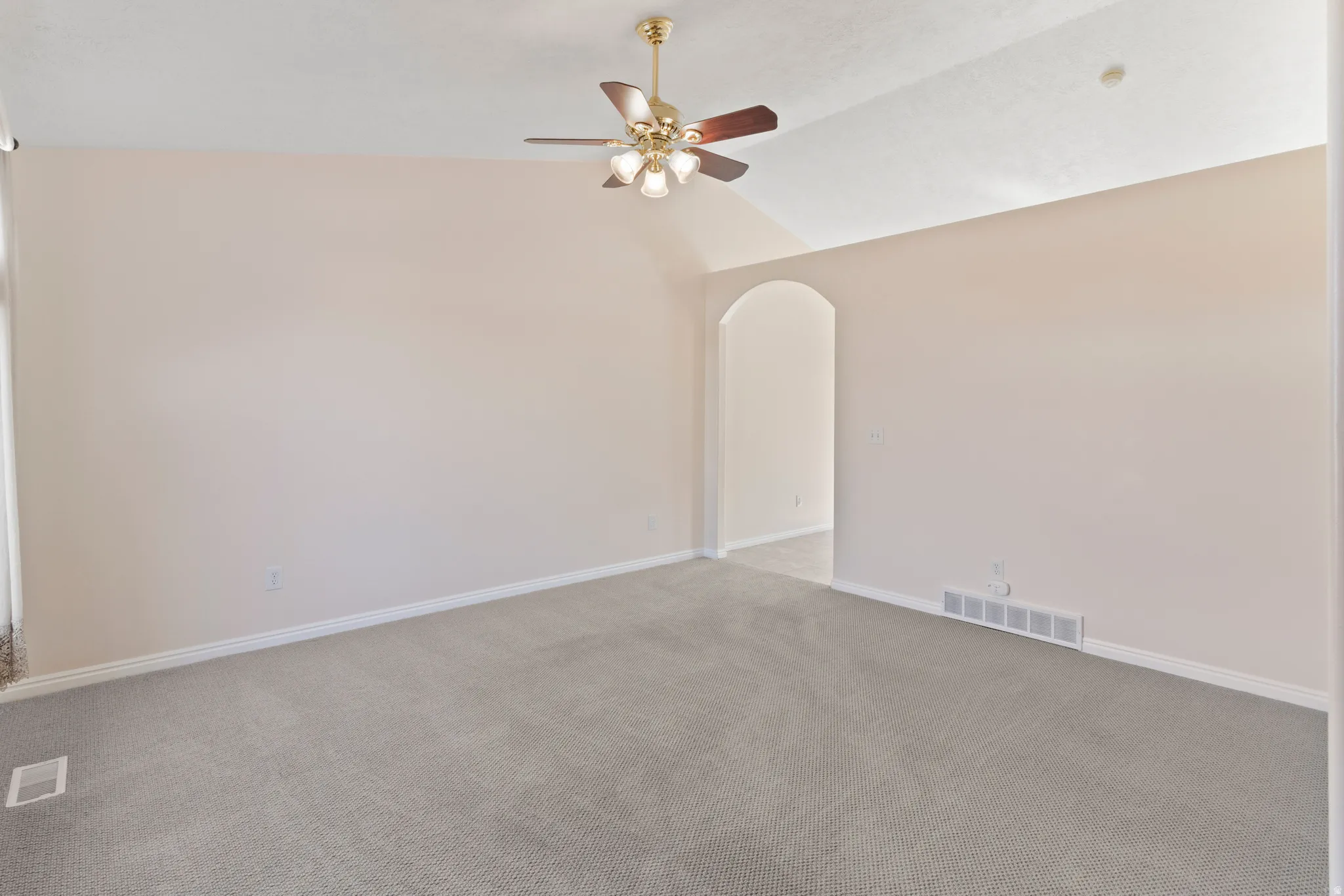 Empty room with arched walkways, lofted ceiling, ceiling fan, and carpet