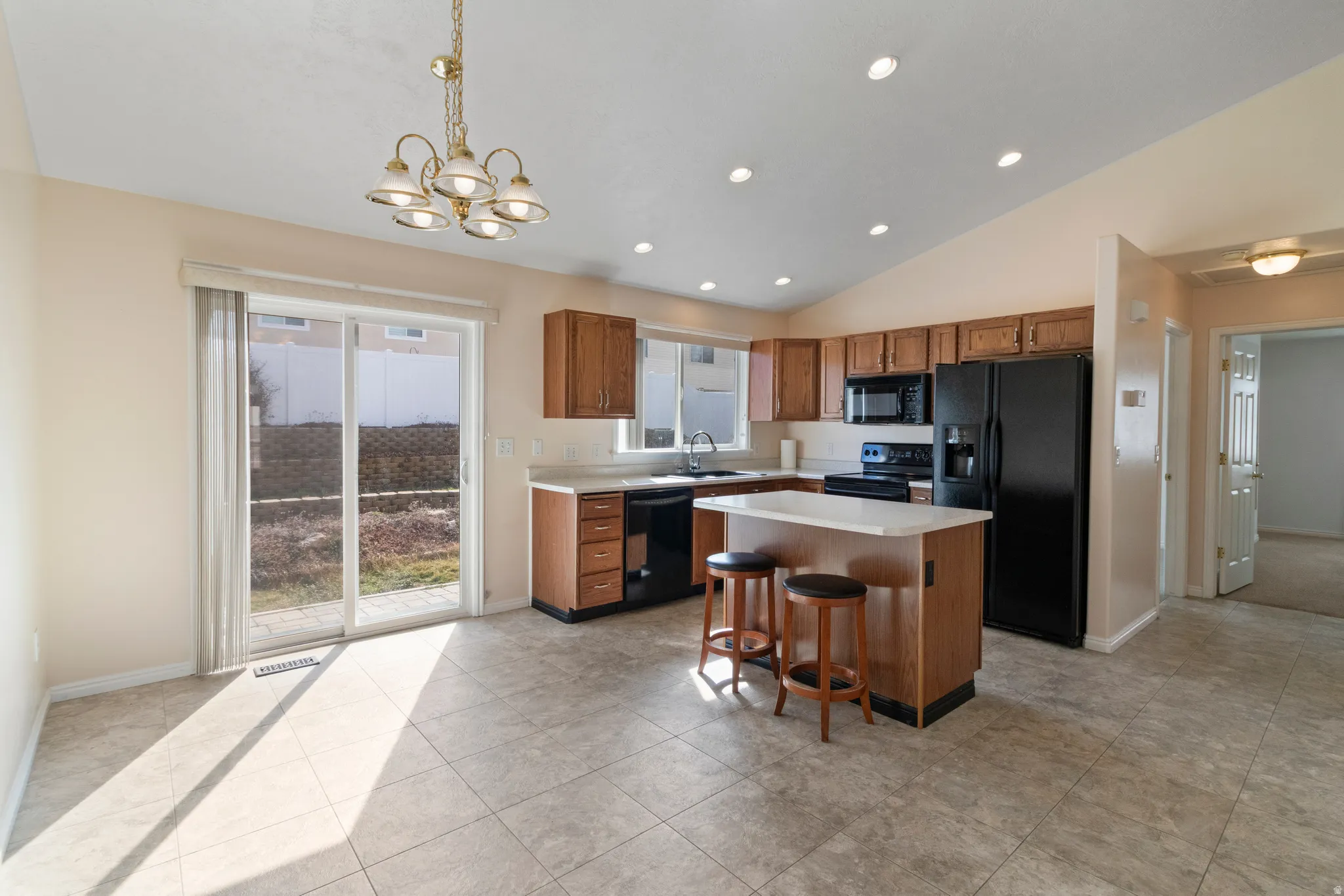 Kitchen featuring black appliances, light countertops, hanging lights, a kitchen island, and wood finish cabinets