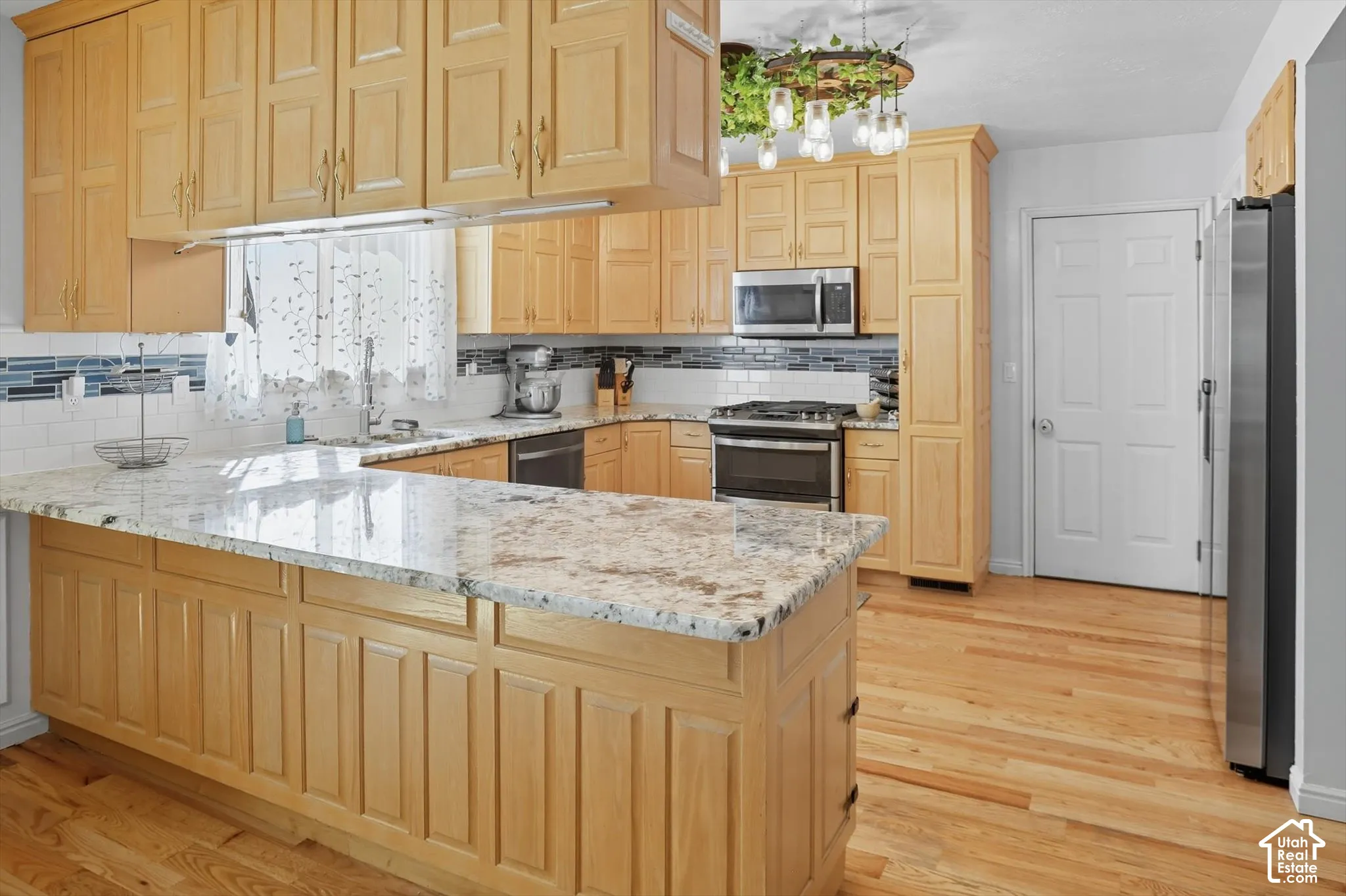 Kitchen with light wood finish cabinets, a peninsula, light stone countertops, and tasteful backsplash