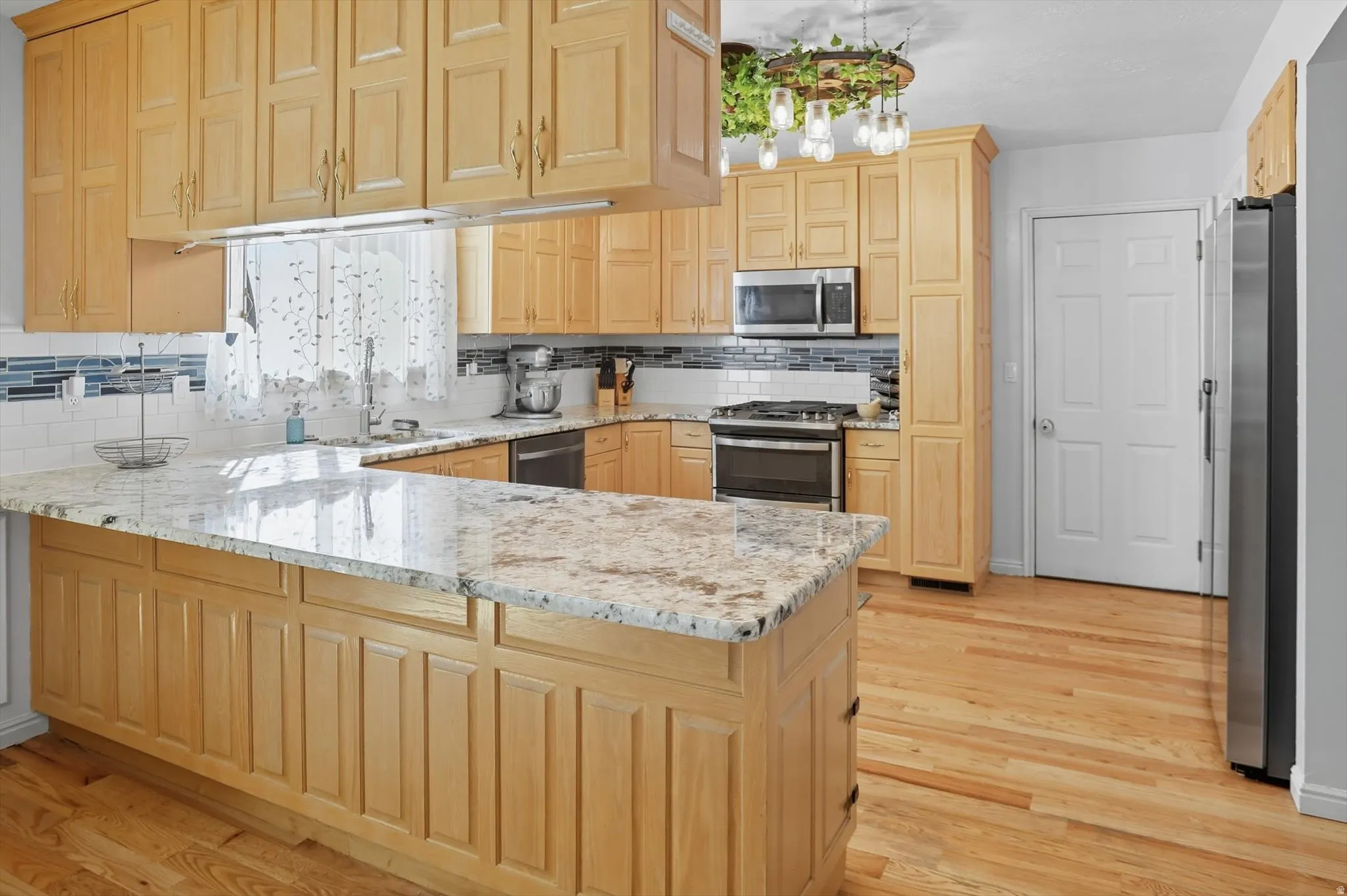 Kitchen with light wood finish cabinets, a peninsula, light stone countertops, and tasteful backsplash