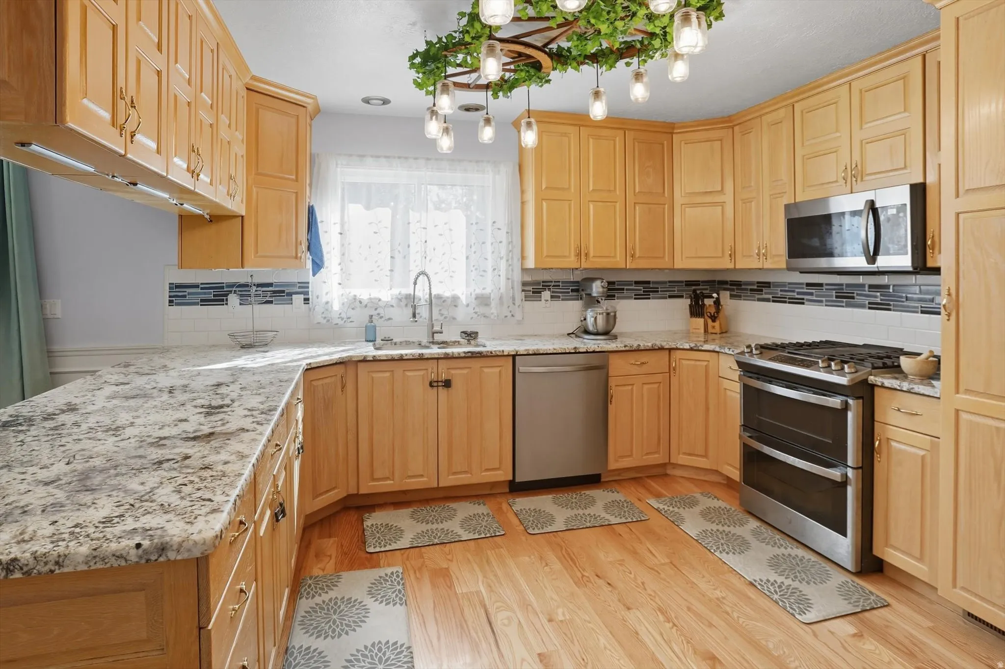 Kitchen featuring stainless steel appliances, light stone counters, light wood finish cabinets, light wood-style flooring, and backsplash