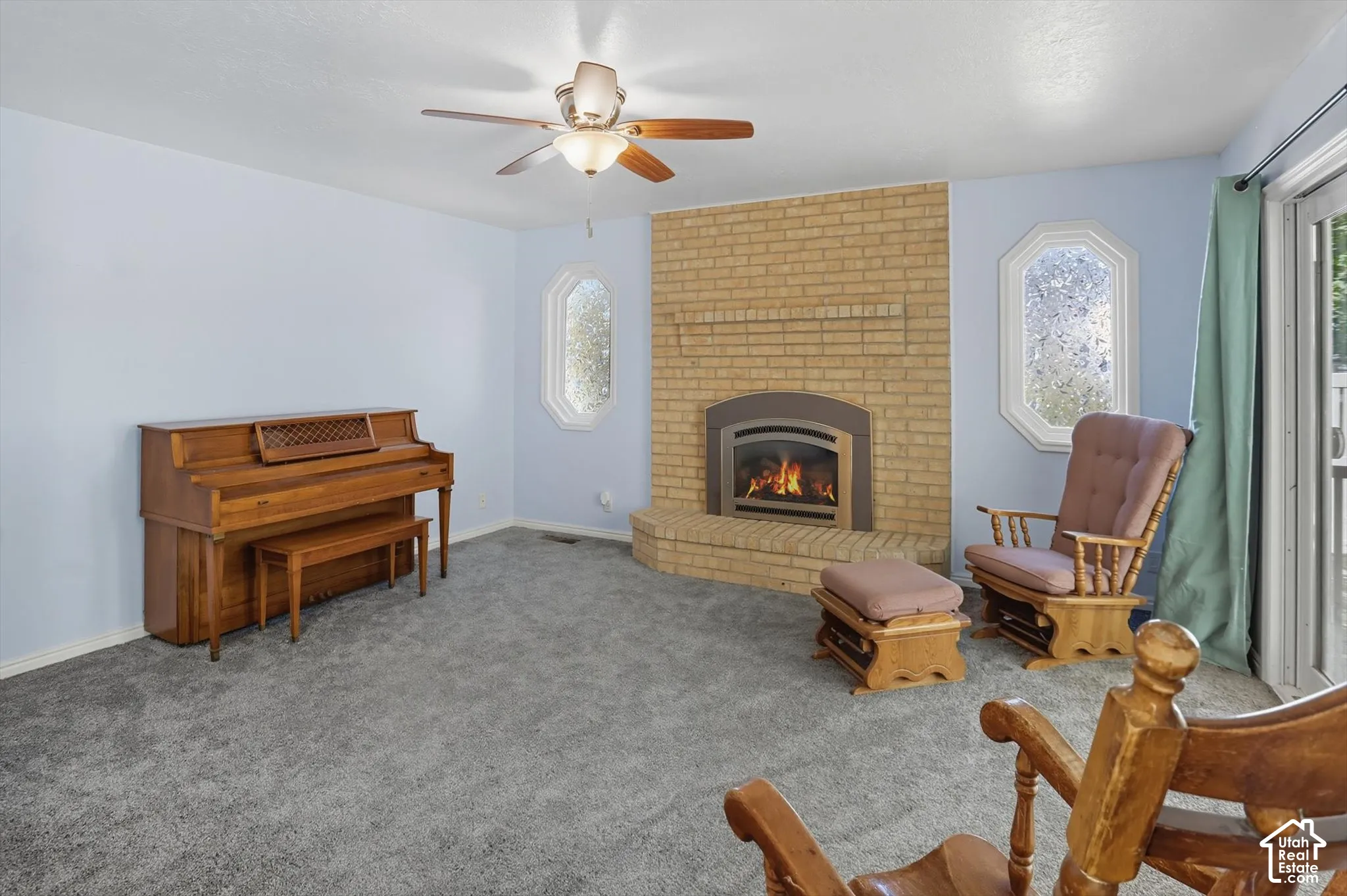 Living area with a ceiling fan, a brick fireplace, and carpet flooring