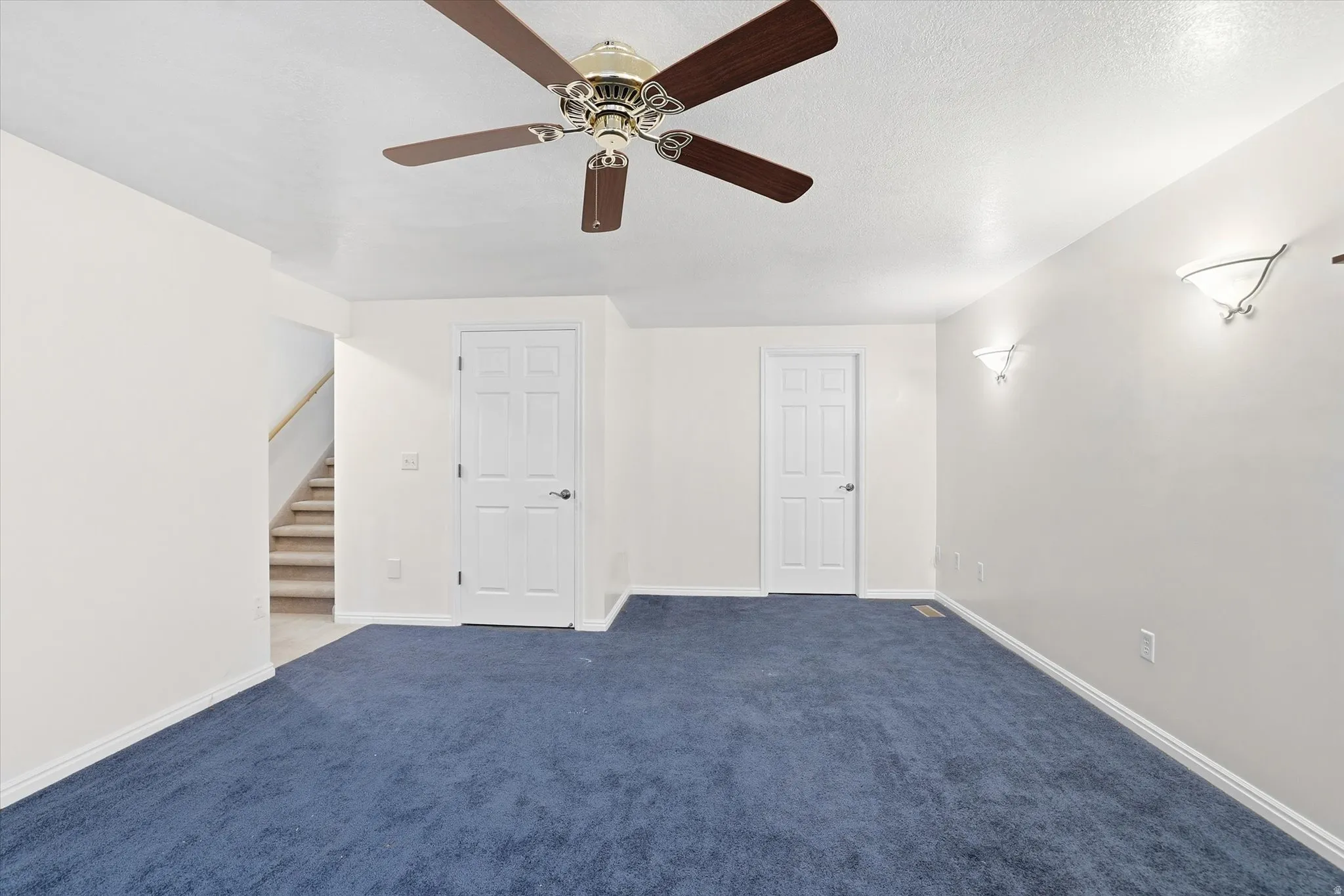 Carpeted spare room featuring ceiling fan and stairway