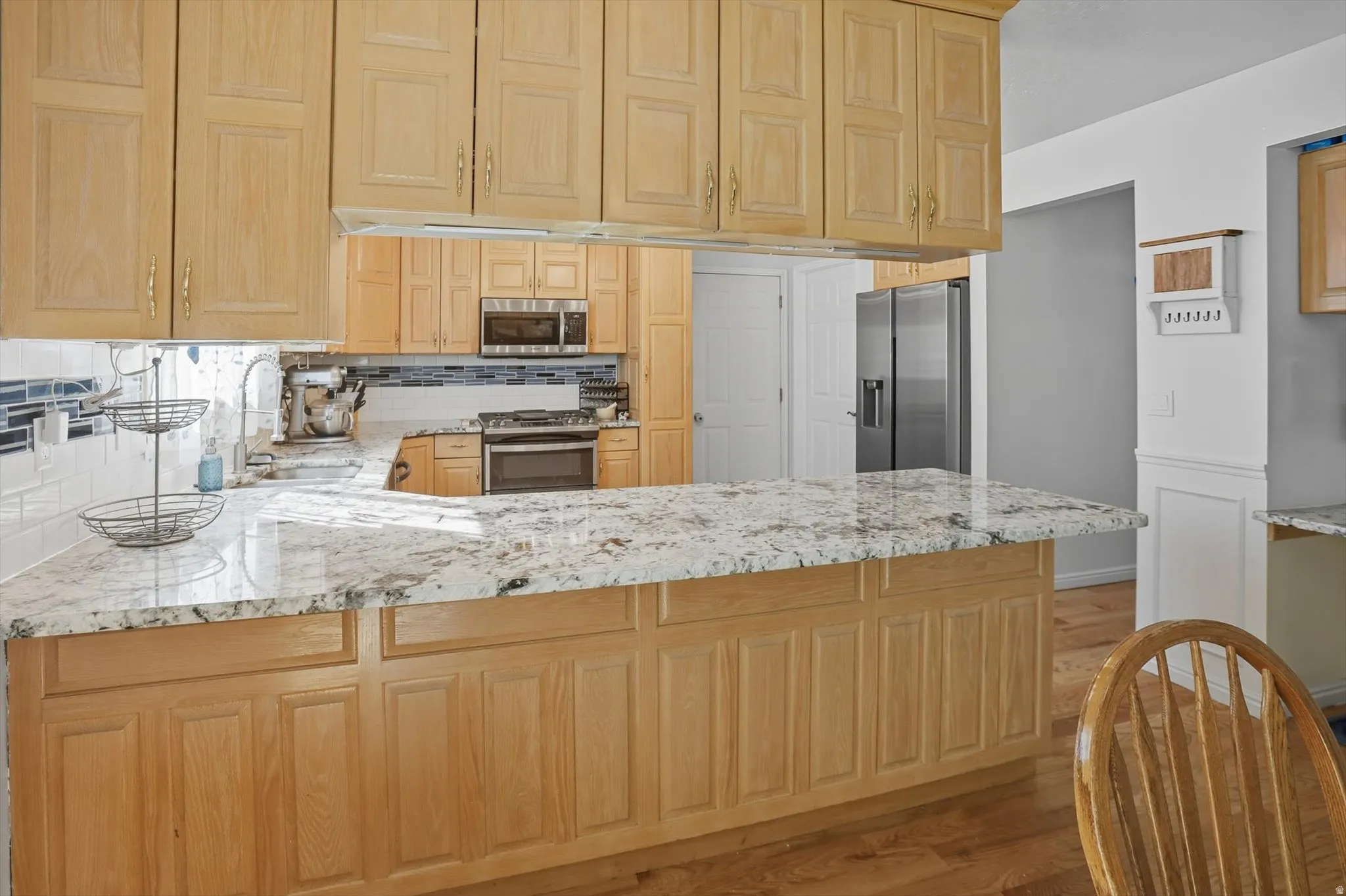 Kitchen with decorative backsplash, light stone countertops, stainless steel appliances, light wood-type flooring, and light wood finish cabinetry