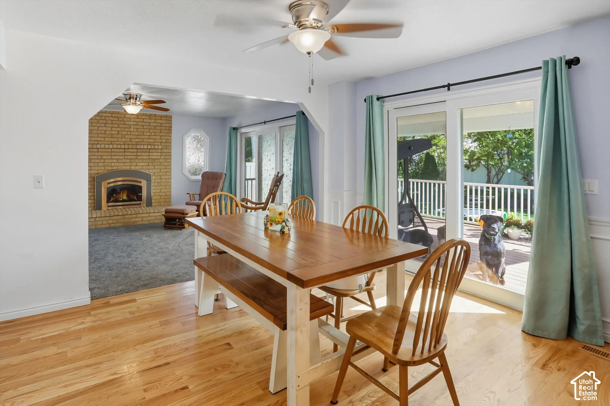 Dining area featuring a ceiling fan, a brick fireplace, light wood-style flooring, and a wainscoted wall