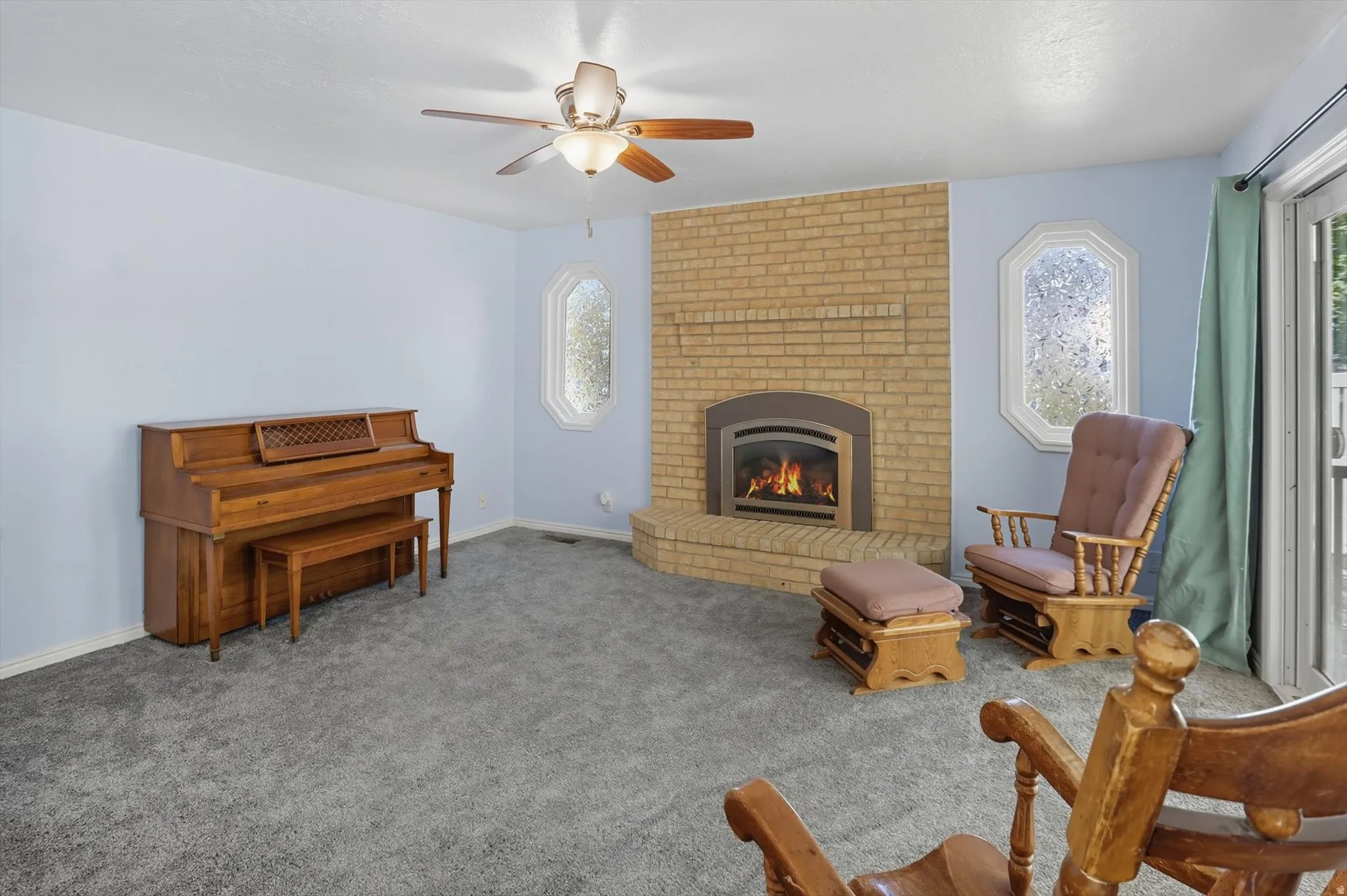 Living area with a ceiling fan, a brick fireplace, and carpet flooring