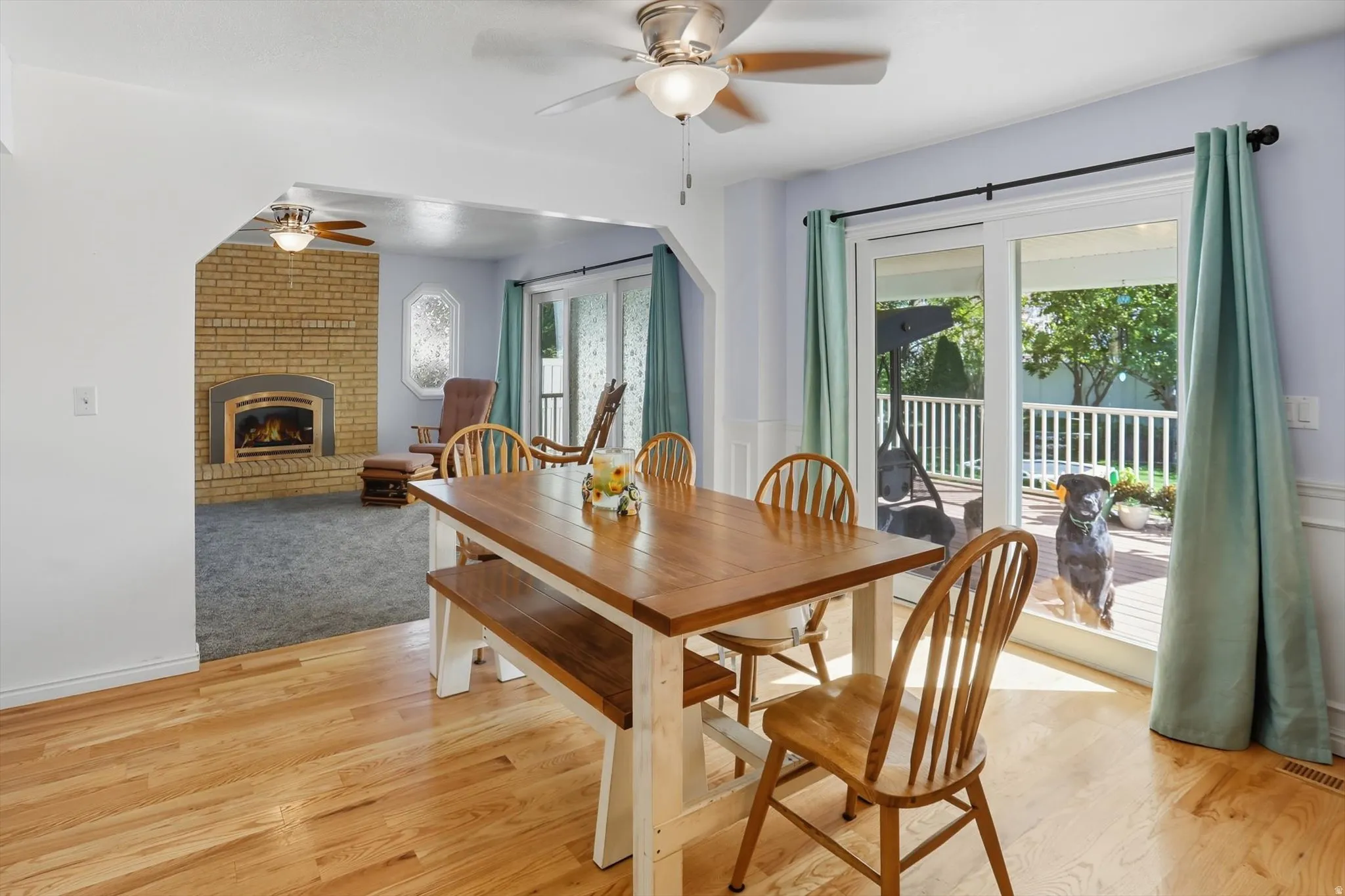 Dining area featuring a ceiling fan, a brick fireplace, light wood-style flooring, and a wainscoted wall