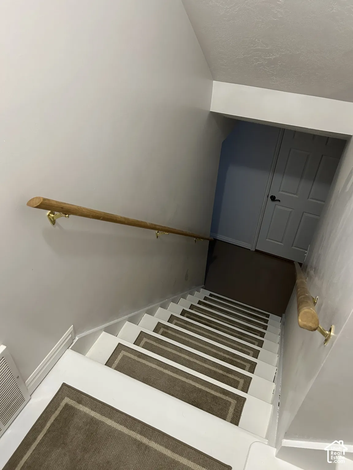 Staircase featuring white risers, carpeted treads, and wood-finish handrails with brass-tone hardware