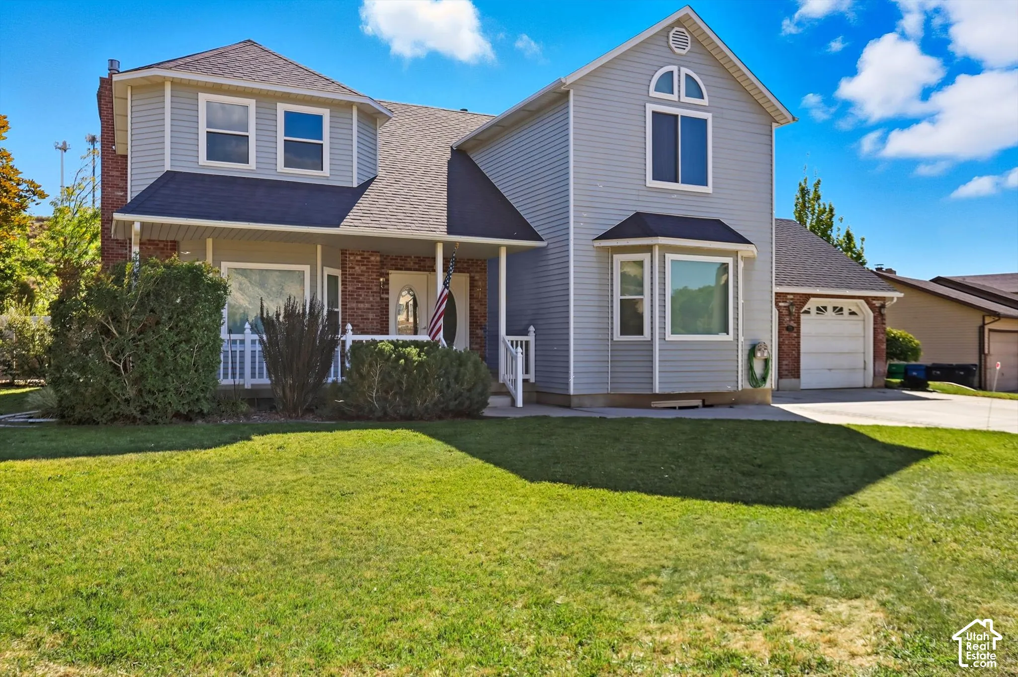 Traditional-style house with roof with shingles, a front lawn, covered porch, concrete driveway, and brick siding