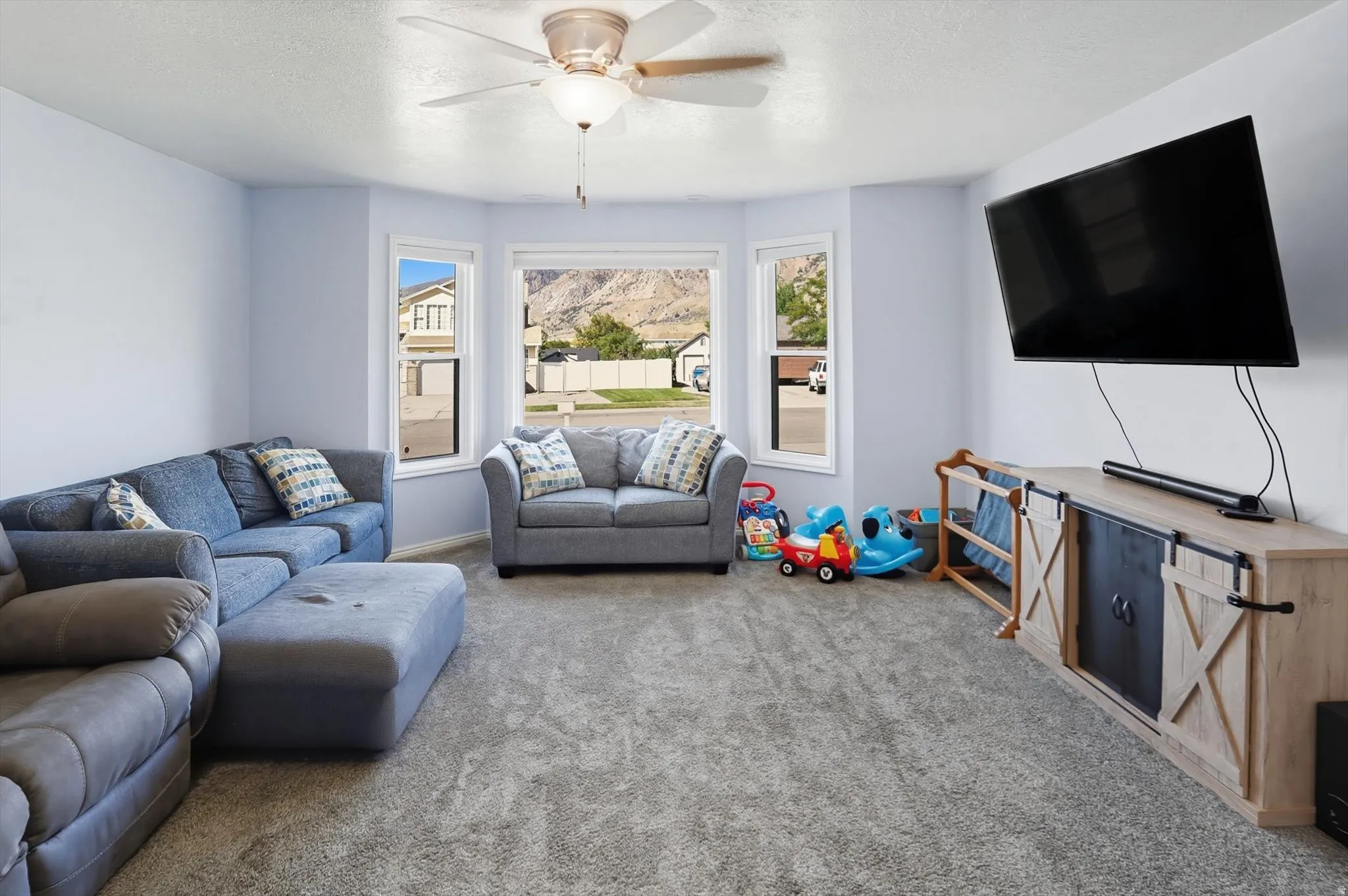 Living area with a ceiling fan, carpet floors, and a textured ceiling