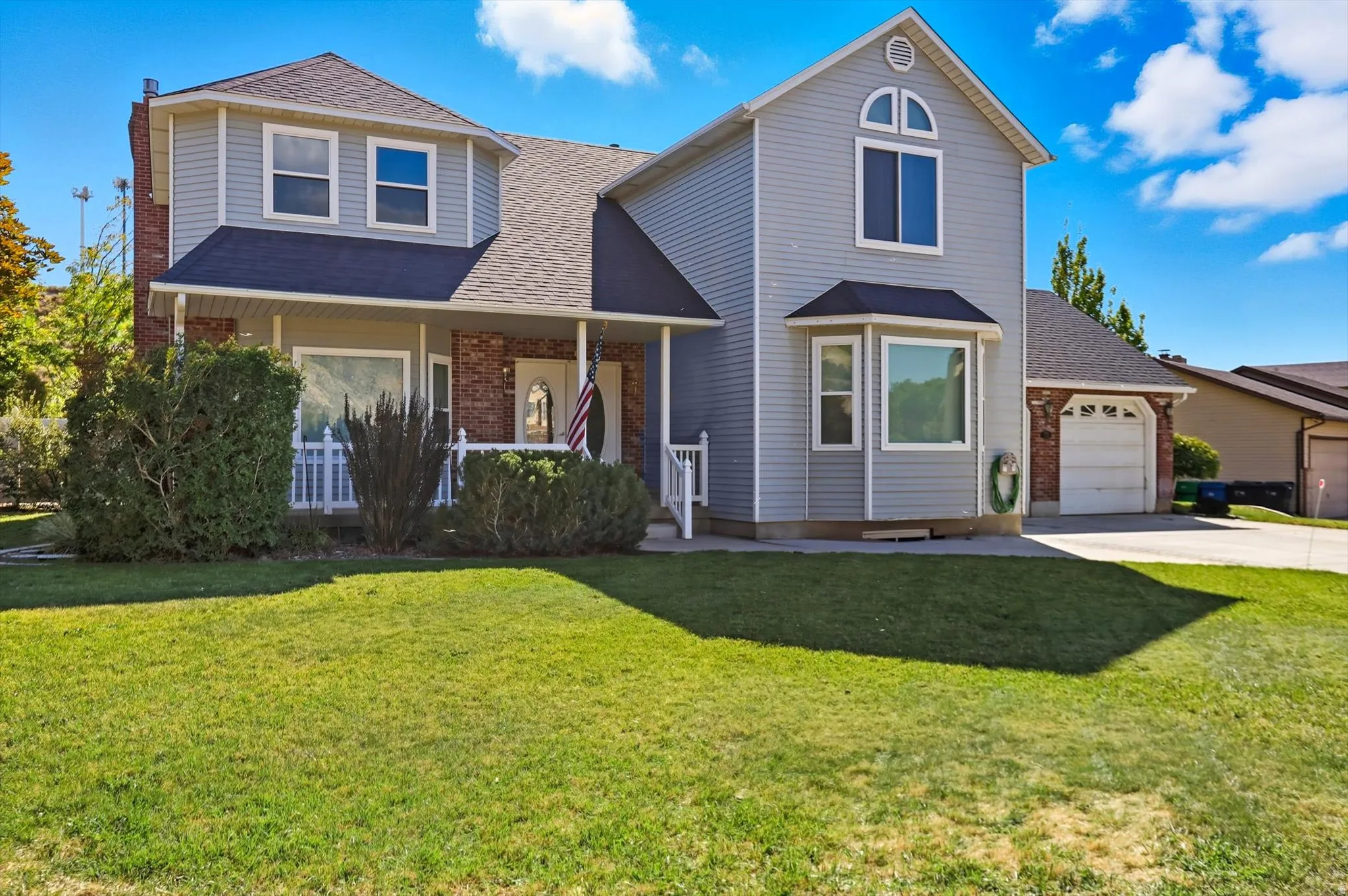 Traditional-style house with roof with shingles, a front lawn, covered porch, concrete driveway, and brick siding