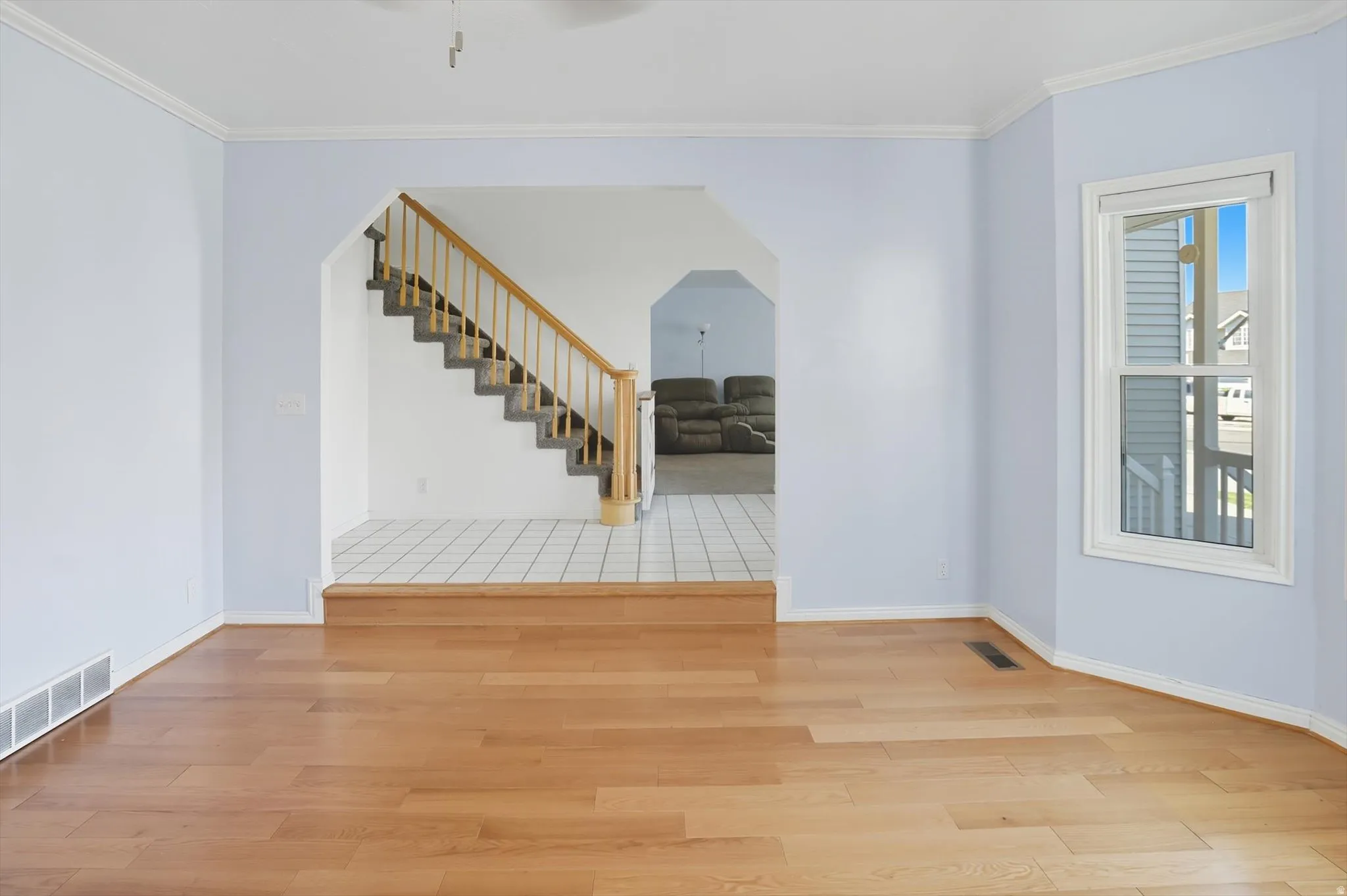 Empty room featuring light wood-style floors, ornamental molding, and arched walkways