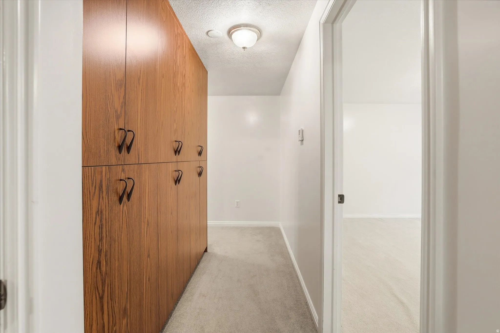 Hallway featuring a textured ceiling and light colored carpet