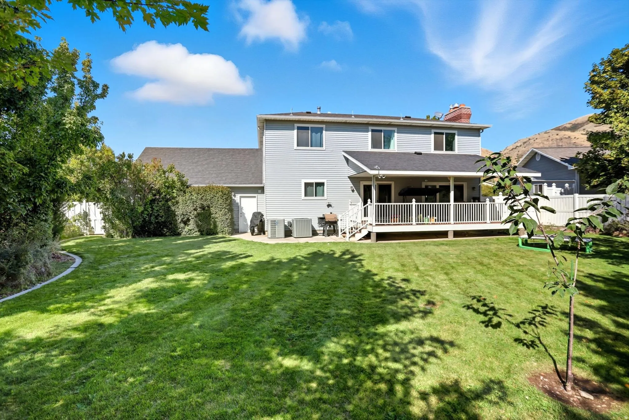 Rear view of property featuring a fenced backyard, a chimney, a deck, and roof with shingles
