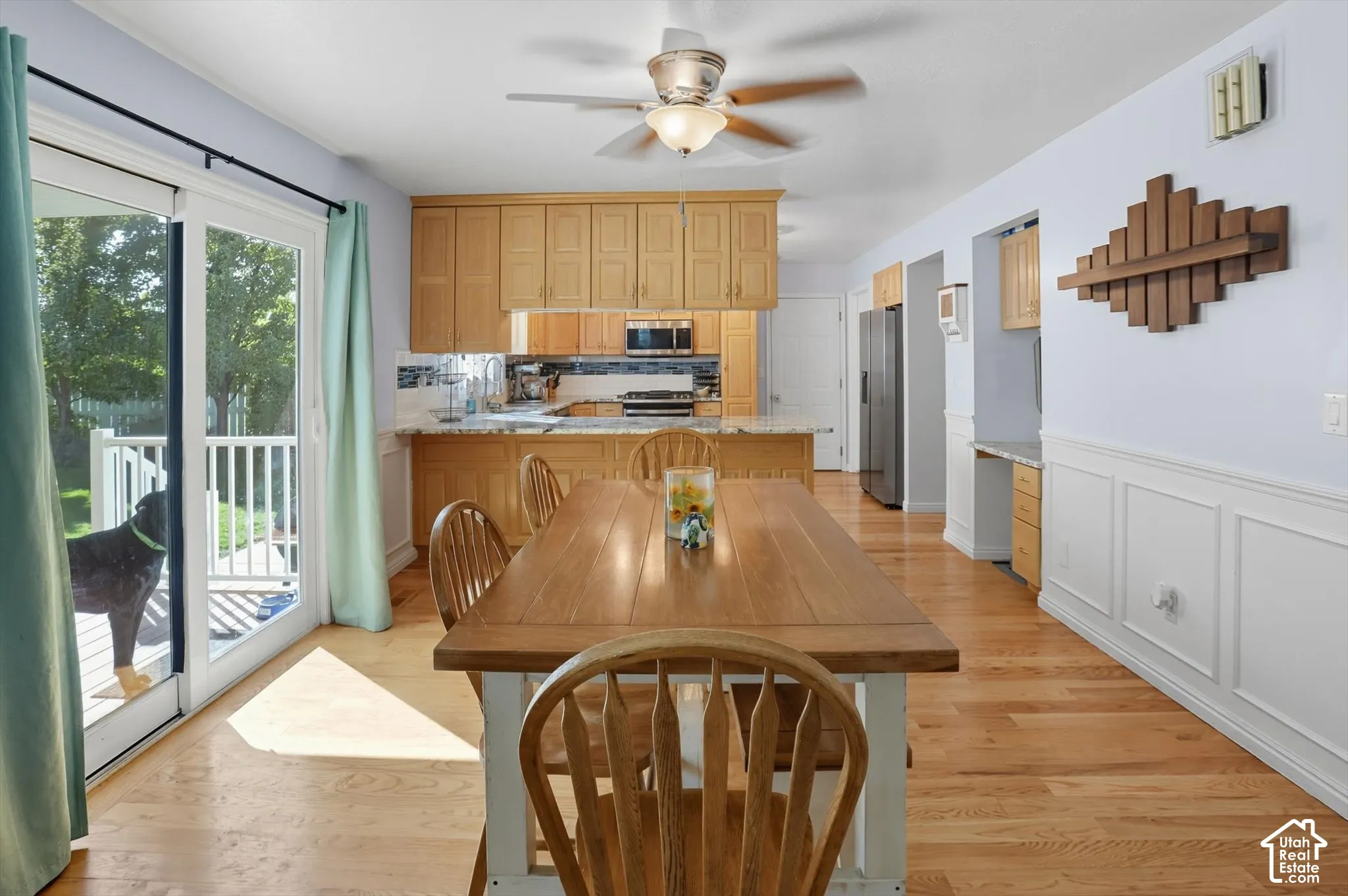 Dining room with light wood-type flooring, ceiling fan, a wainscoted wall, and a decorative wall