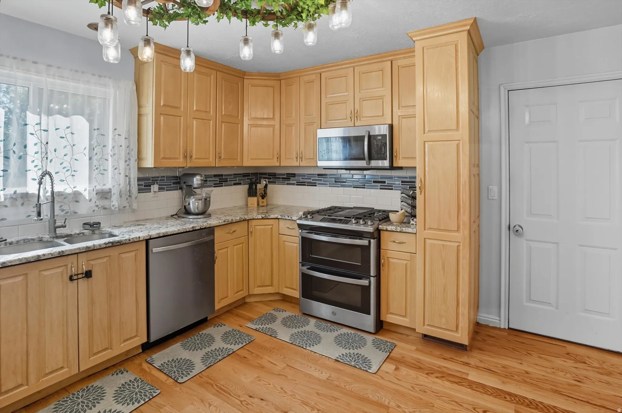 Kitchen featuring stainless steel appliances, light stone counters, tasteful backsplash, light wood-style flooring, and light wood finish cabinets