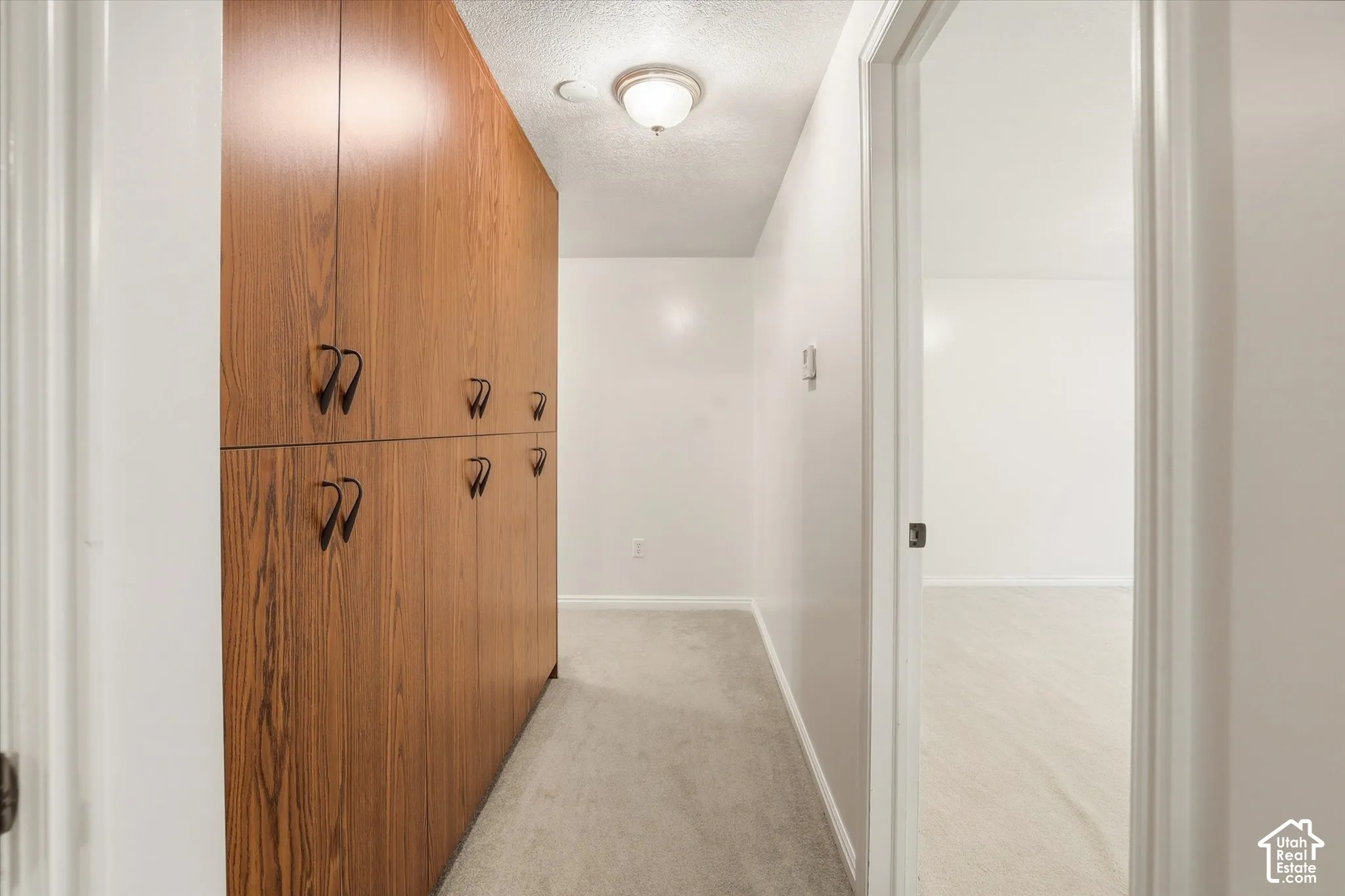 Hallway featuring a textured ceiling and light colored carpet