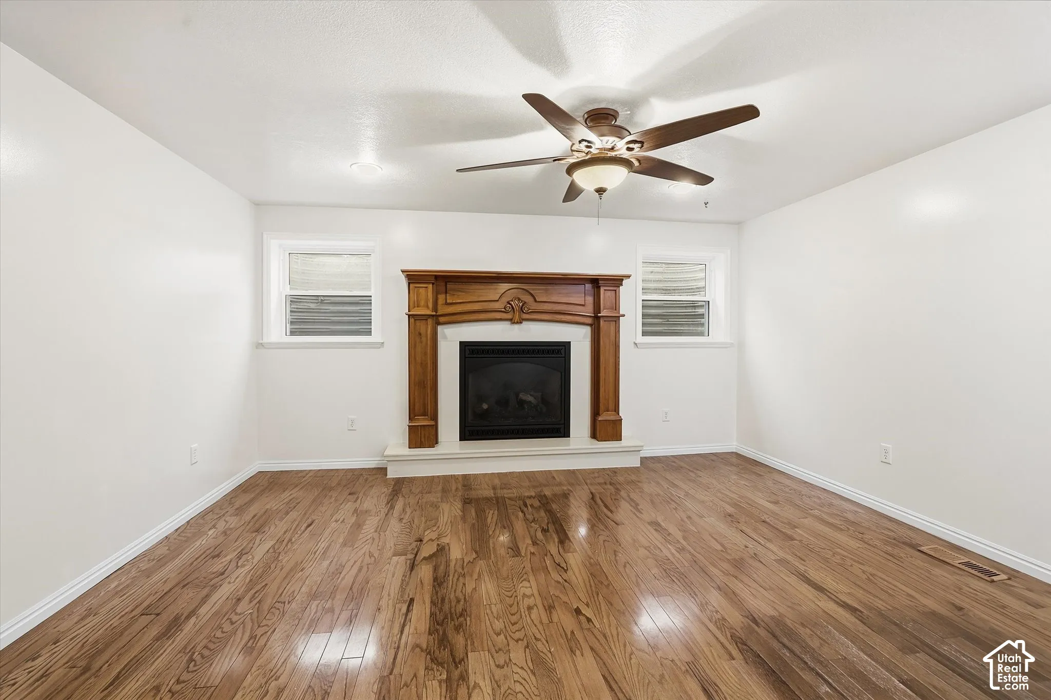 Unfurnished living room featuring wood-type flooring, ceiling fan, plenty of natural light, and a fireplace with raised hearth