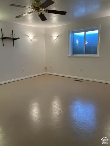 Room featuring smooth-finish flooring, a metal-finish ceiling fan with integrated lighting, dual wall-mounted sconces, and a sliding window