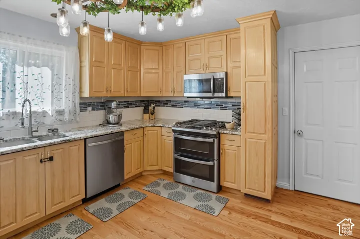 Kitchen featuring stainless steel appliances, light stone counters, tasteful backsplash, light wood-style flooring, and light wood finish cabinets